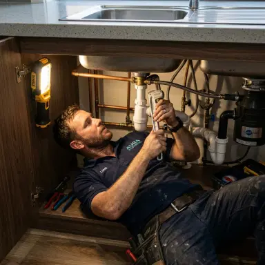 Australian plumber working under a kitchen sink